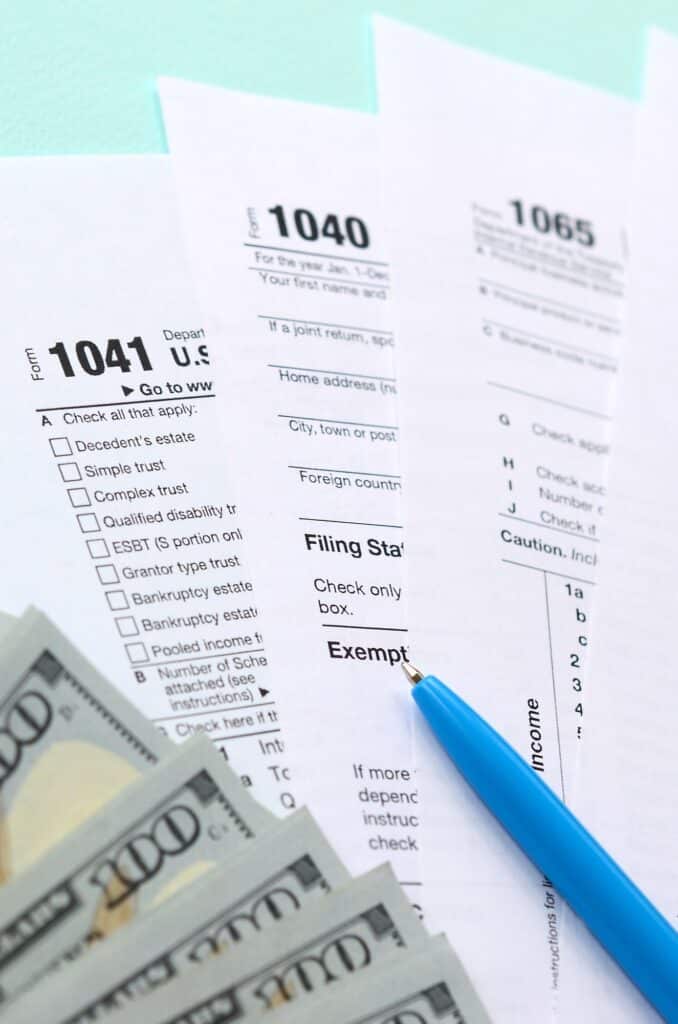 Tax forms lies near hundred dollar bills and blue pen on a light blue background. Income tax return.