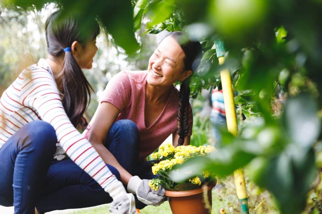 Happy asian mother and daughter smiling, wearing gloves and working in garden