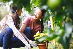 Happy asian mother and daughter smiling, wearing gloves and working in garden